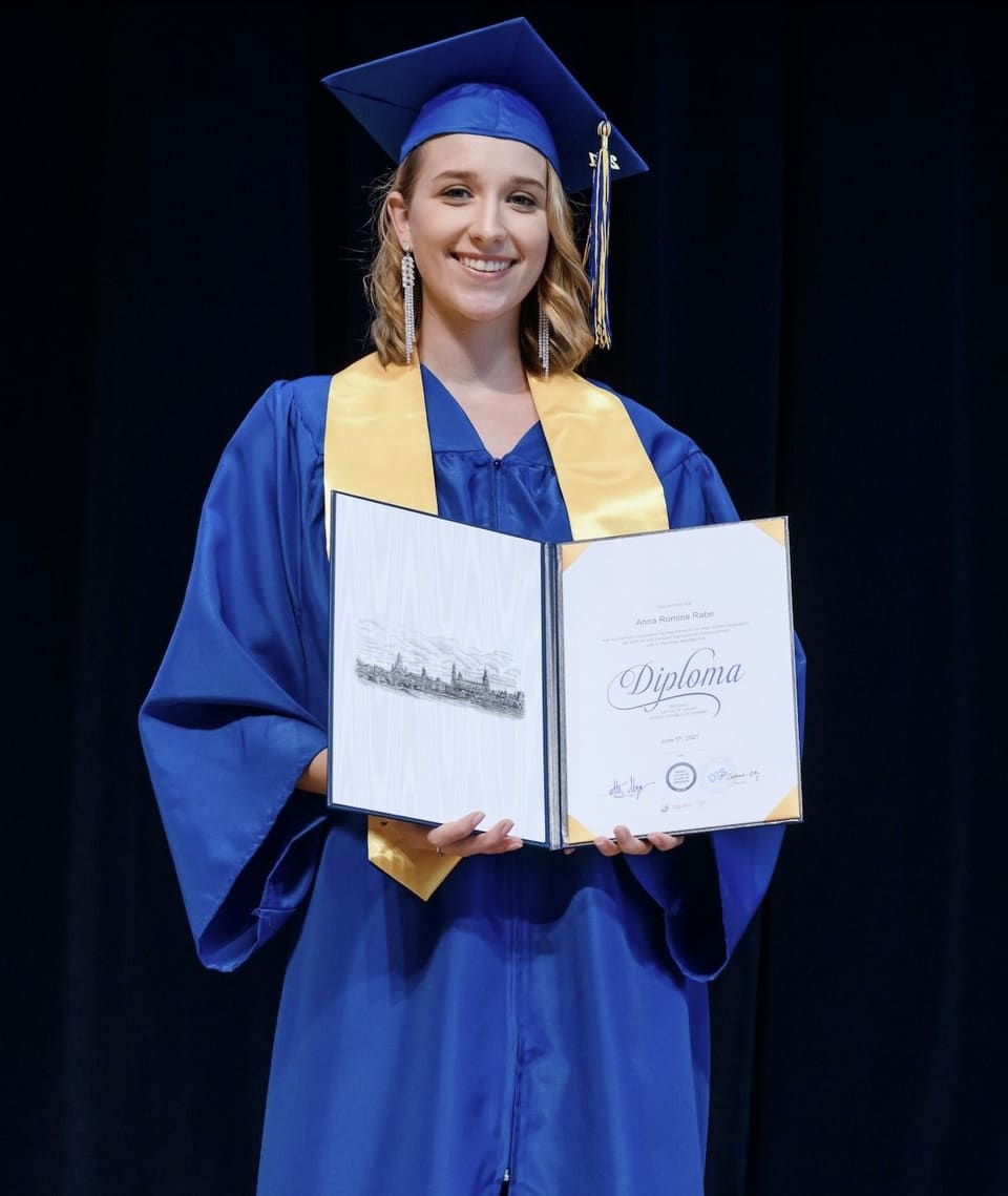 Anna at her high school graduation, in a blue gown holding a diploma
